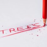 Close-up of a red pencil writing 'stress' on paper, symbolizing pressure and creativity.