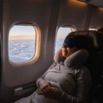 Comment Bien Dormir en Voyage : 8 Astuces Anti-Décalage 2026 2 Voyageur dormant paisiblement dans un avion avec masque de sommeil et coussin cervical, illustrant le repos en voyage